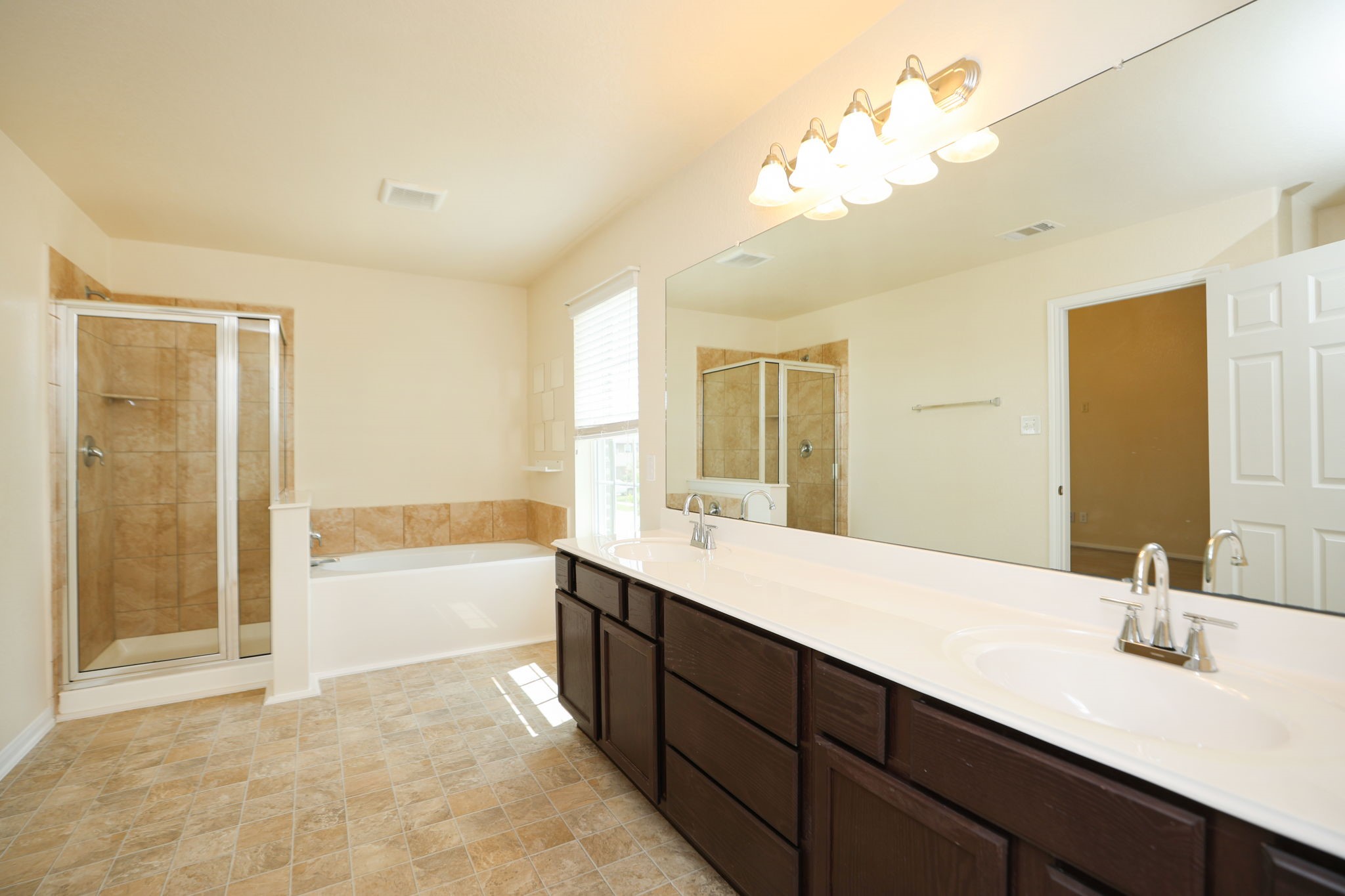 18402 Spruce Tree Line Trail Houston, TX 77084 - Photo 18 of 30 This spacious bathroom features a large double vanity with dark wood cabinets, a wide mirror, a glass-enclosed shower, and a separate bathtub. The neutral tiles and ample natural light create a bright and inviting atmosphere.