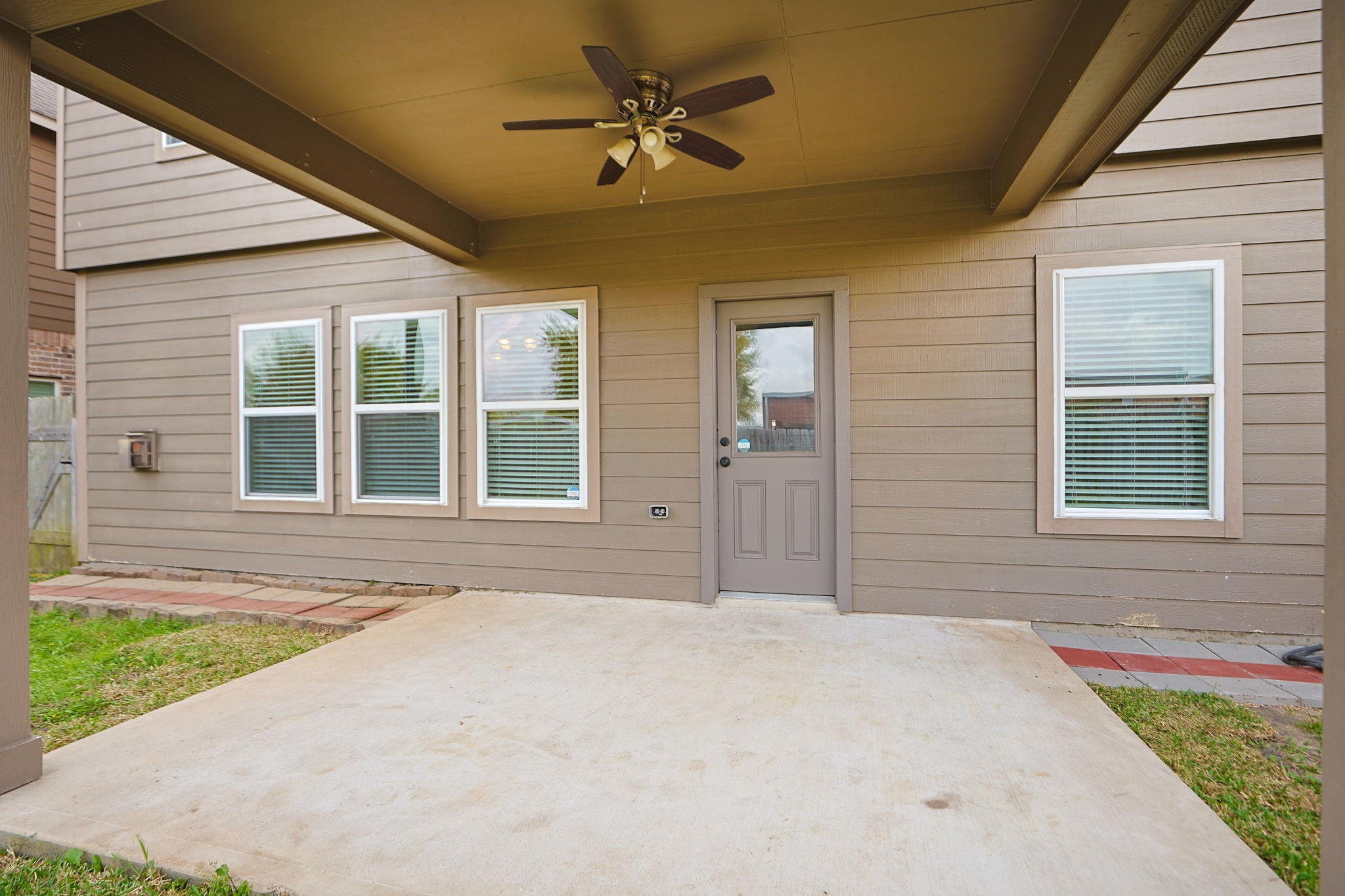 18402 Spruce Tree Line Trail Houston, TX 77084 - Photo 25 of 30 This photo showcases a covered patio with a ceiling fan, adjacent to a home's exterior with multiple windows and a door. Ideal for outdoor relaxation and entertainment.