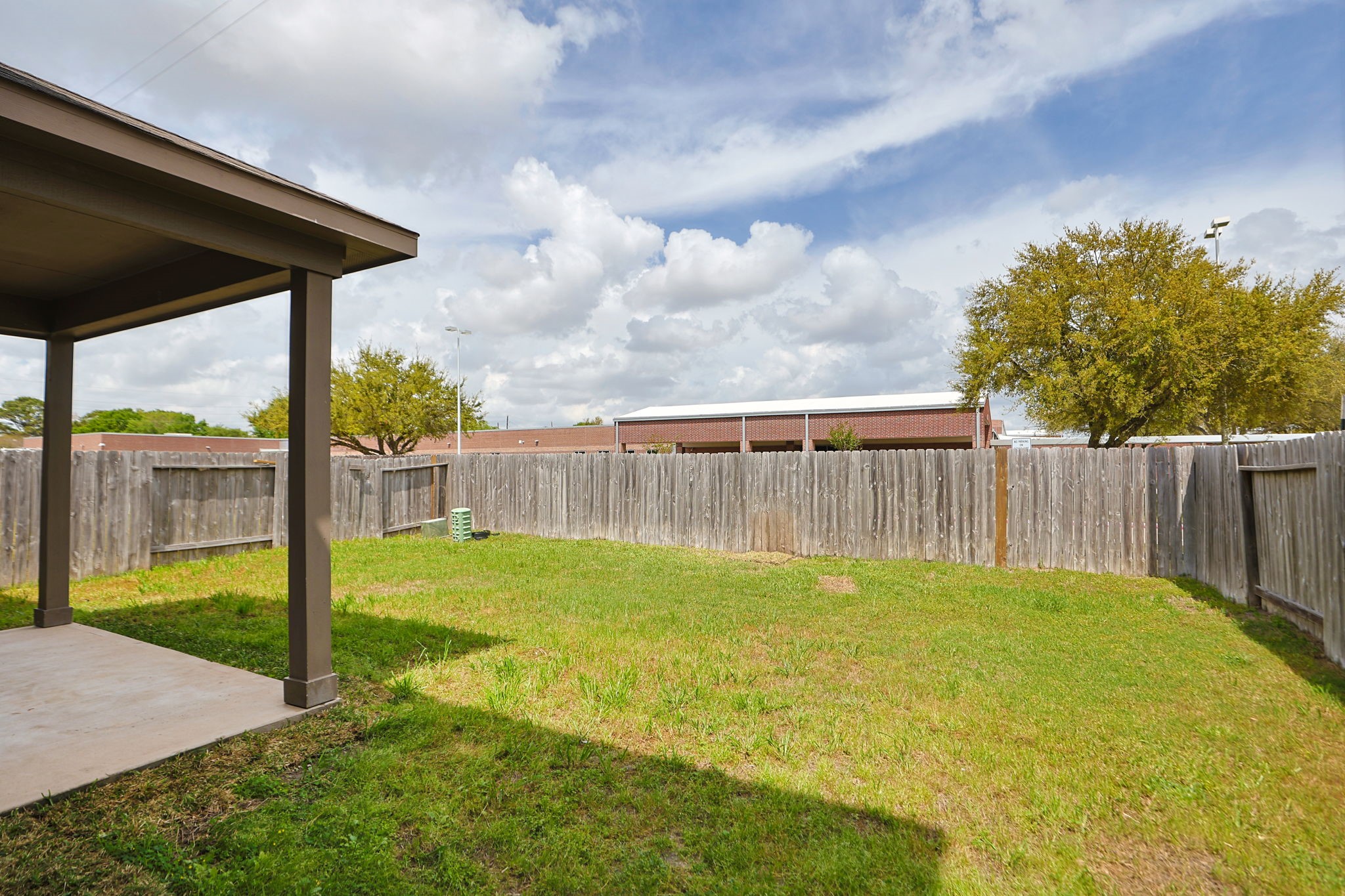 18402 Spruce Tree Line Trail Houston, TX 77084 - Photo 26 of 30 This backyard features a covered patio area, a wooden fence for privacy, and a grassy lawn, ideal for outdoor activities and relaxation. The space is open and sunlit, with a clear view of the sky.