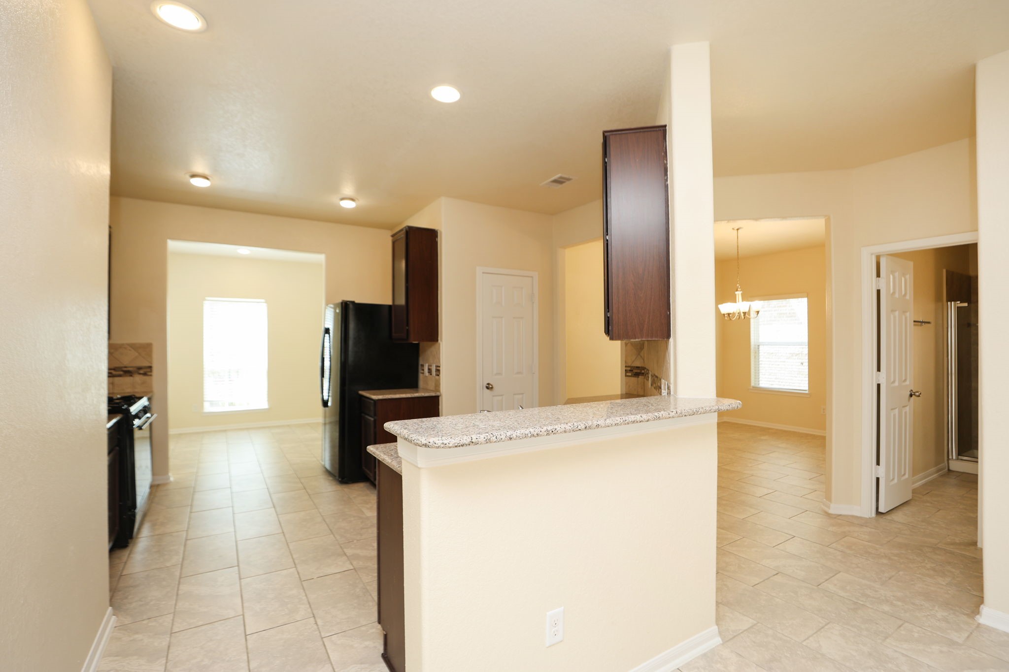 18402 Spruce Tree Line Trail Houston, TX 77084 - Photo 5 of 30 This photo showcases a bright, open kitchen with modern appliances, granite countertops, and tile flooring. It features a breakfast bar and leads into a dining area with natural light.