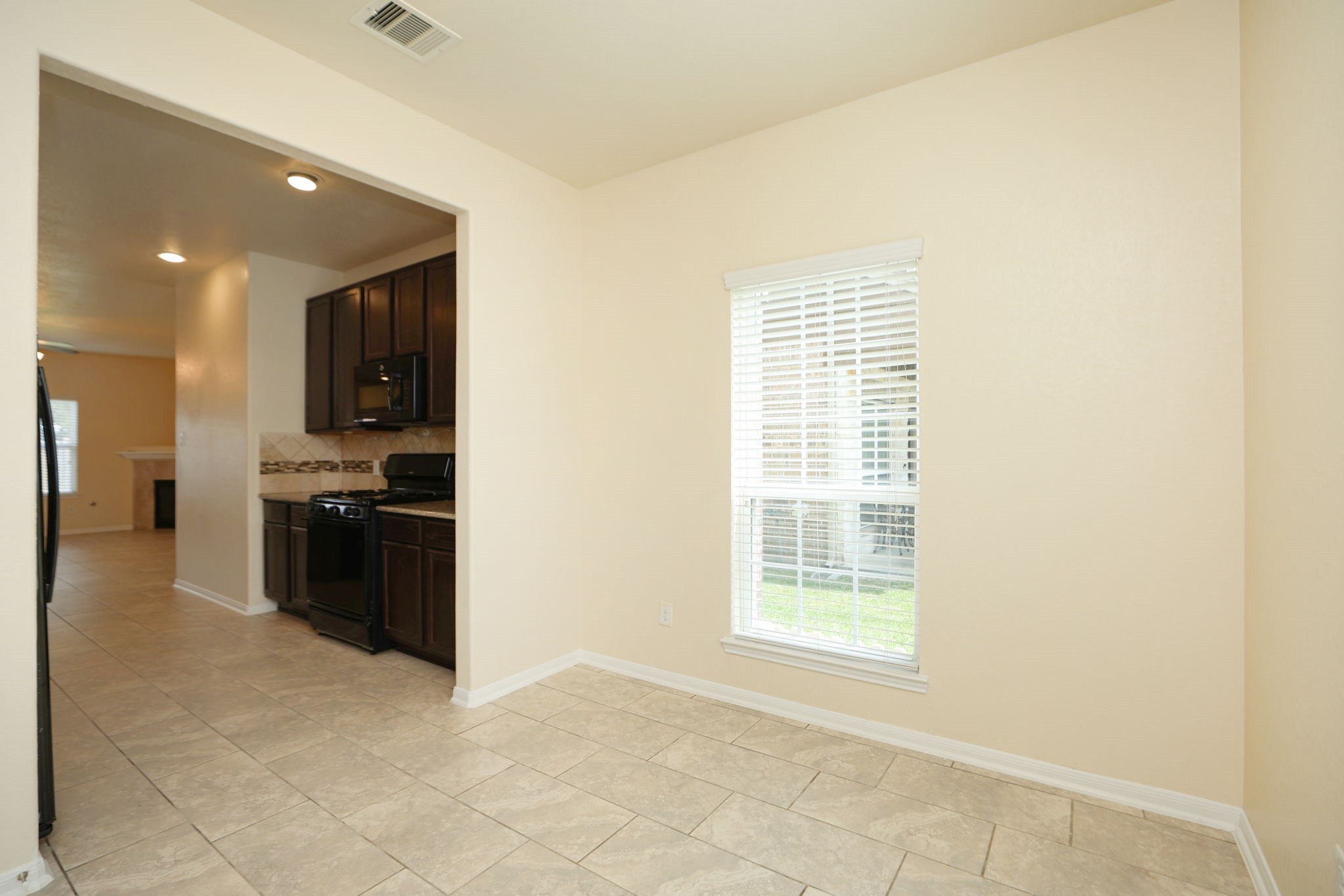 18402 Spruce Tree Line Trail Houston, TX 77084 - Photo 9 of 30 Bright dining area with large window, adjacent to a modern kitchen featuring dark wood cabinets and black appliances. The open layout extends into a spacious living area with tiled flooring.