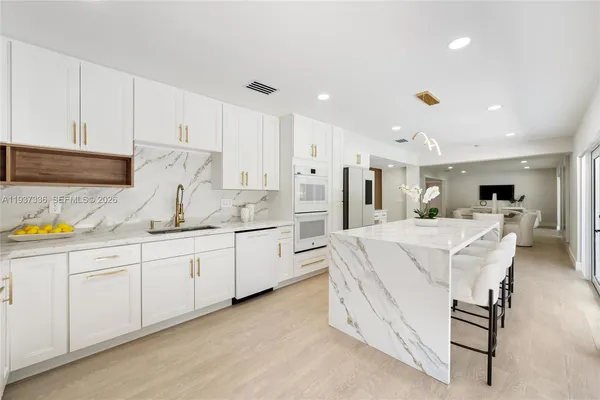 a large white kitchen with granite countertop a large window and a sink