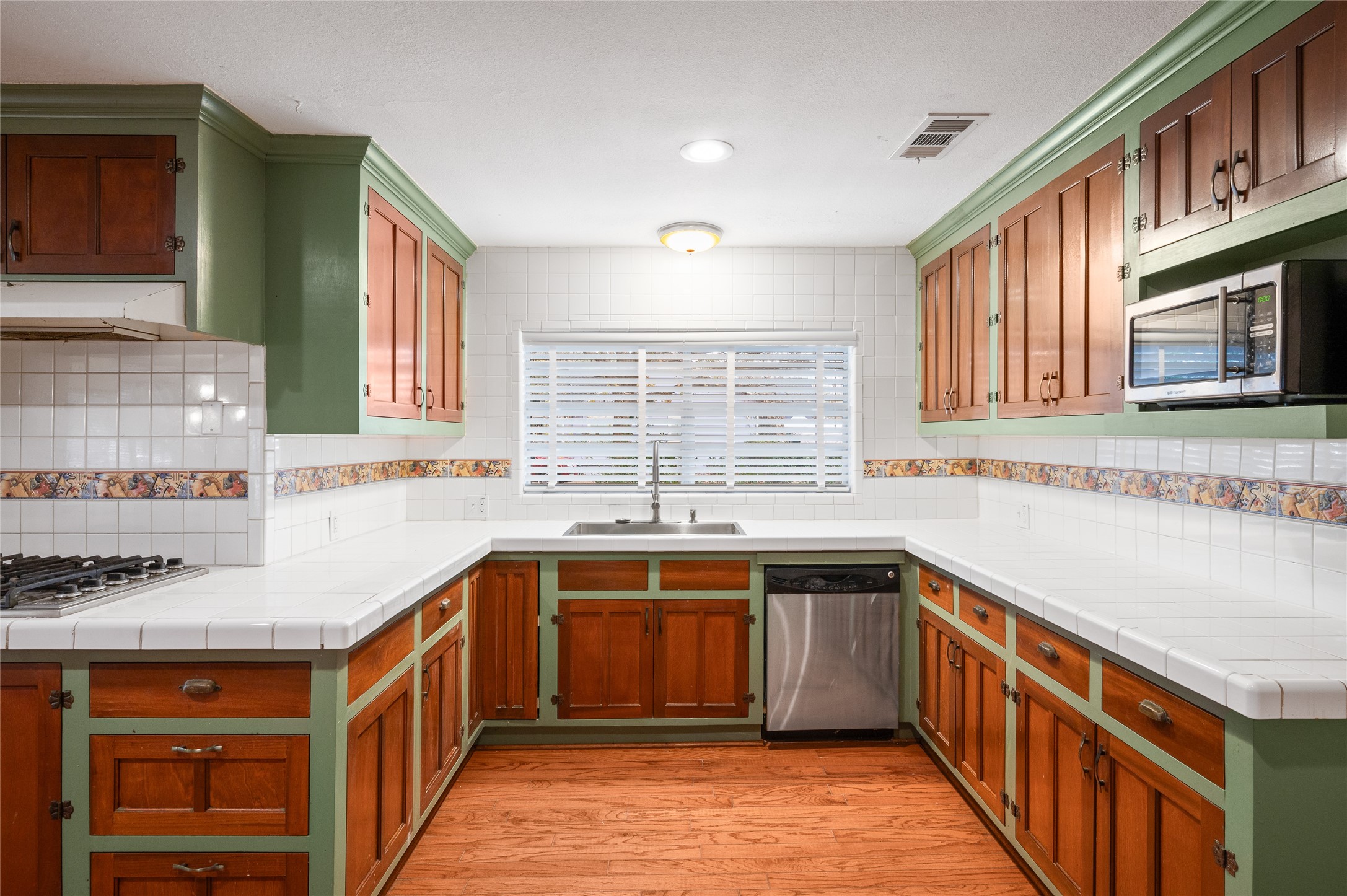 405 Hohldale Street Houston, TX 77091 - Photo 7 of 39 View of the kitchen sink area with window overlooking the yard, tile countertops, stainless dishwasher, and plentiful cabinet storage.