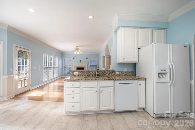 a kitchen with granite countertop a refrigerator a stove a sink and white cabinets with wooden floor