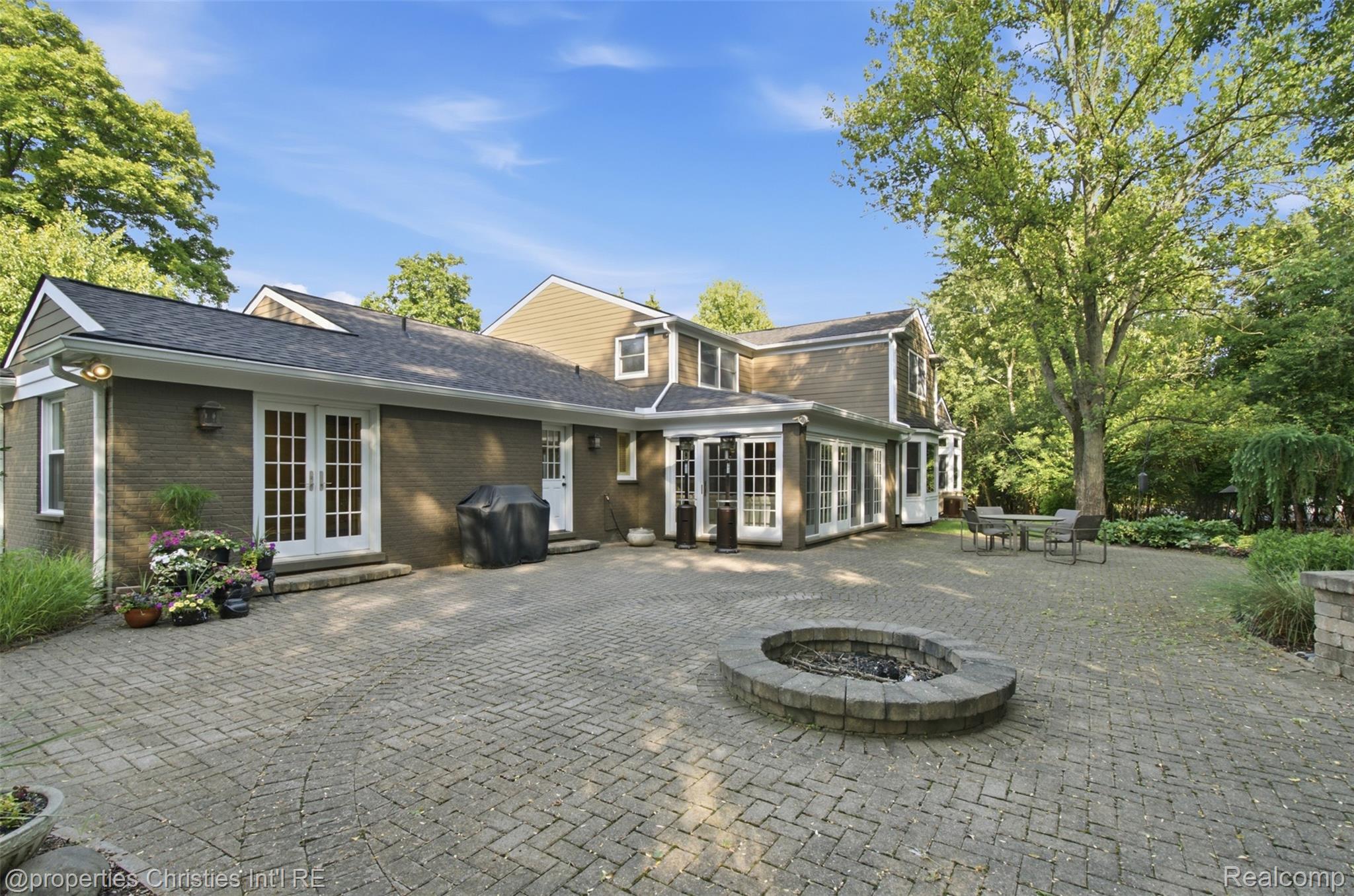 25235 Canterbury Road Franklin, MI 48025 - Photo 4 of 56 Expansive brick paver patio featuring a built-in stone fire pit, multiple sets of French doors, and a sunroom with large windows