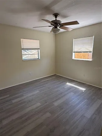 an empty room with wooden floor fan and windows