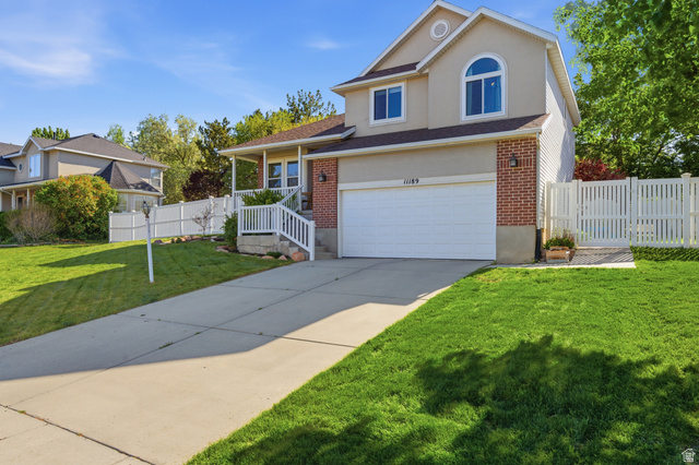 11189 Ohenry Road East Sandy, UT 84070 - Photo 2 of 44 Two-story residence featuring a brick and stucco facade, a two-car garage, an arched window, a covered front porch with white railing, and a white picket fence