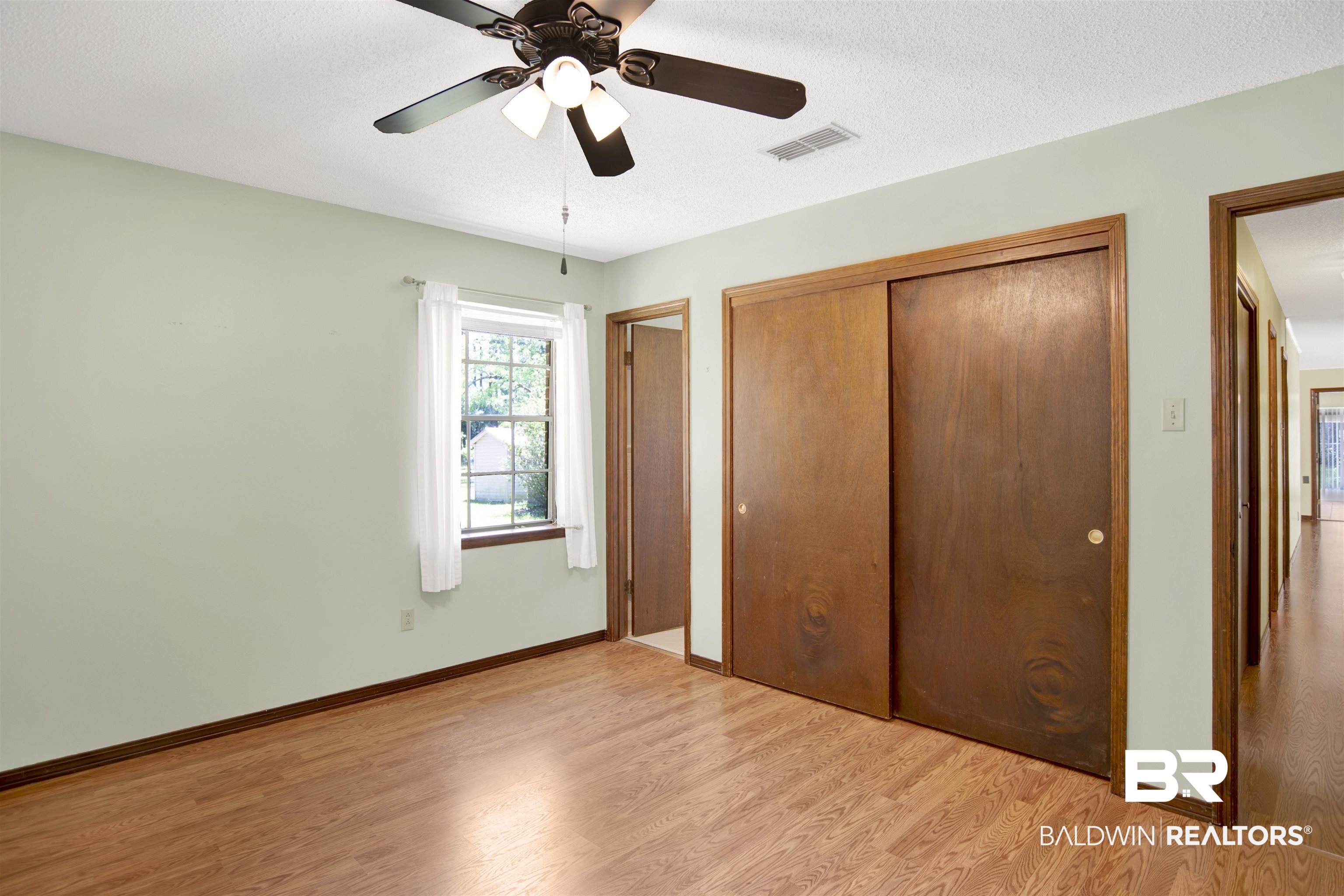 30888 Cemetery Road Daphne, AL 36527 - Photo 18 of 36 Bedroom featuring wood-finish flooring, a ceiling fan with integrated lighting, a double-door closet with sliding panels, and a window with white curtains