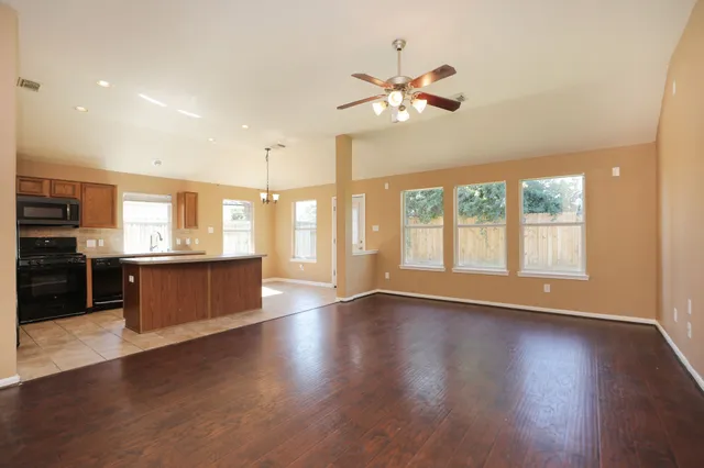 a view of an empty room with wooden floor and a kitchen