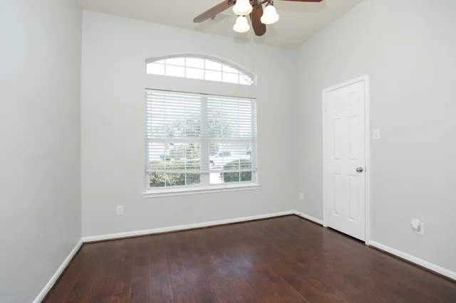 an empty room with wooden floor chandelier fan and windows