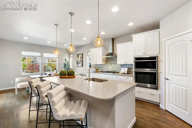 a kitchen with stainless steel appliances granite countertop a stove top oven a sink a dining table and chairs with wooden floor