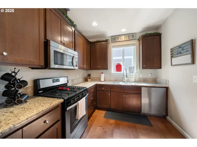 a kitchen with stainless steel appliances granite countertop a refrigerator a sink dishwasher a dining table and chairs with wooden floor