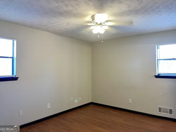 an empty room with wooden floor chandelier fan and windows