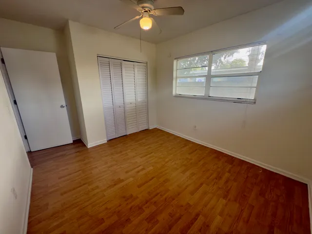 an empty room with wooden floor fan and windows