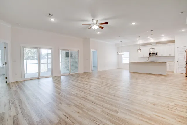 a view of an empty room with wooden floor and a kitchen