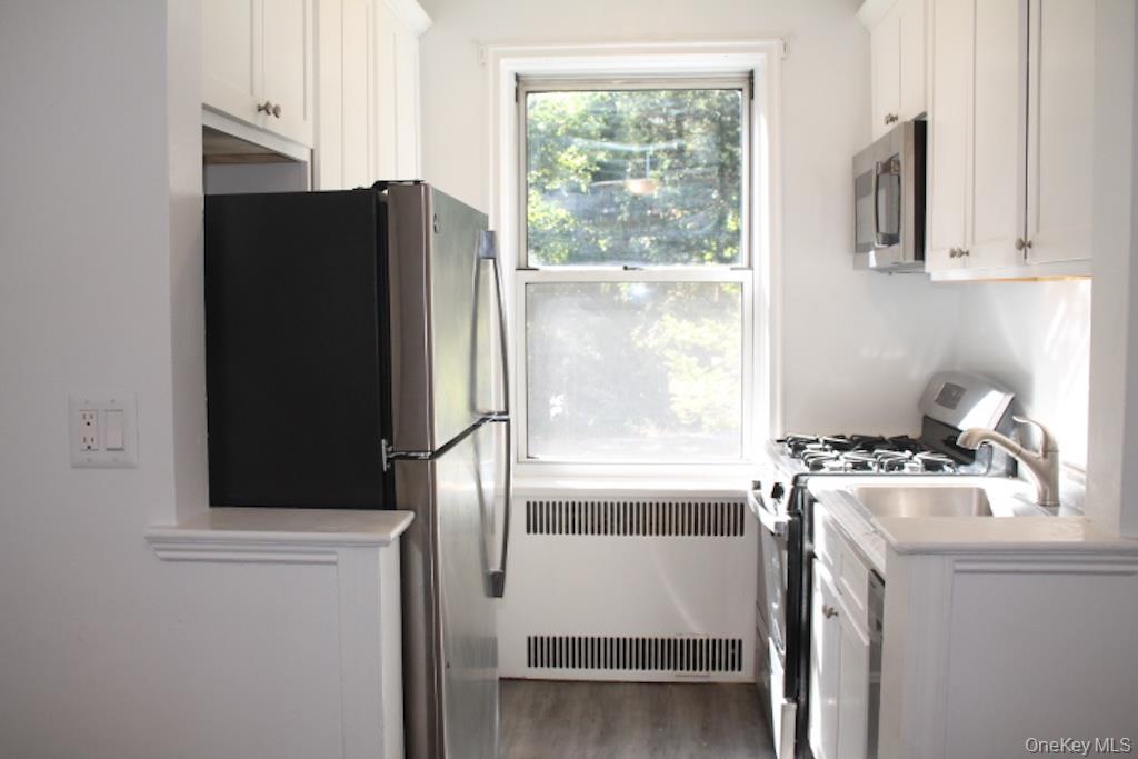 766 Palmer Road, Unit 2F Bronxville, NY 10708 - Photo 8 of 22 Kitchen with white cabinetry, stainless steel appliances, radiator heating unit, and light wood-type flooring