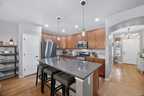 a kitchen with granite countertop a refrigerator a stove a sink a dining table and chairs with wooden floor