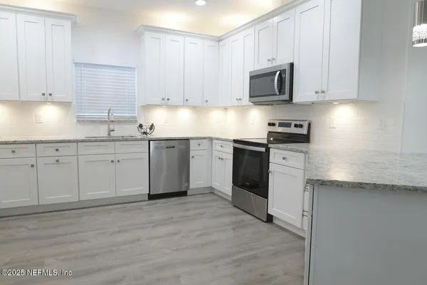 a kitchen with stainless steel appliances granite countertop a stove top oven a sink and white cabinets