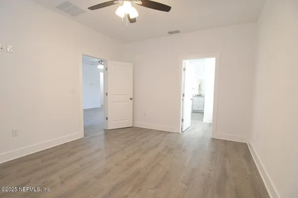 an empty room with wooden floor chandelier fan and windows