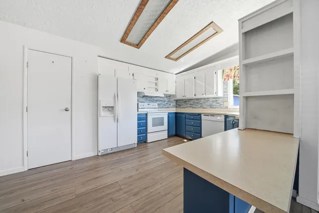 a kitchen with stainless steel appliances granite countertop a refrigerator a sink dishwasher and white cabinets with wooden floor