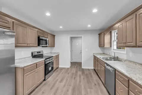 a kitchen with stainless steel appliances granite countertop wooden cabinets a sink dishwasher a stove and a refrigerator