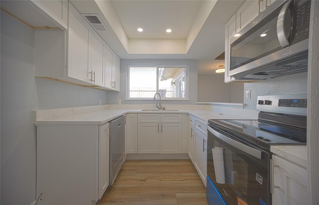 733 Intrepid Drive Garland, TX 75043 - Photo 9 of 25 Kitchen with appliances with stainless steel finishes, white cabinetry, light countertops, light wood-type flooring, and a textured wall