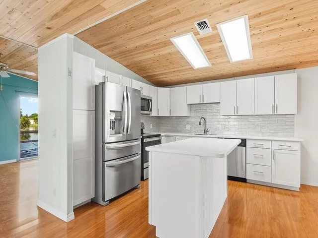 a kitchen with stainless steel appliances granite countertop a refrigerator a sink dishwasher a stove and white countertops with wooden floor