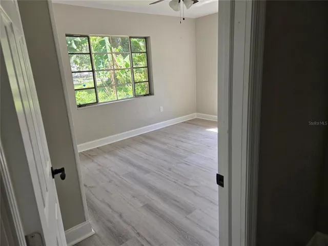 an empty room with wooden floor fan and windows
