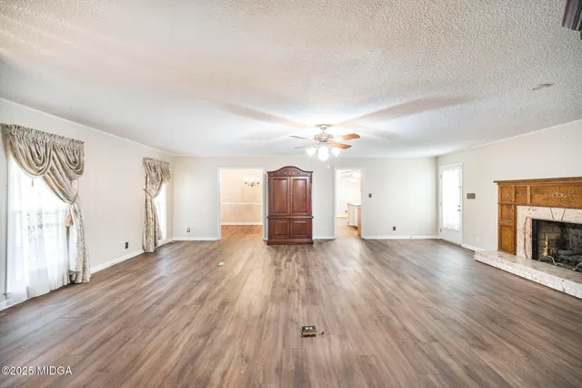 an empty room with wooden floor fireplace and windows