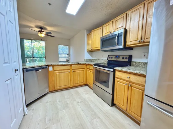 a kitchen with stainless steel appliances granite countertop wooden cabinets a sink a stove a refrigerator a microwave oven with cabinets and wooden floor