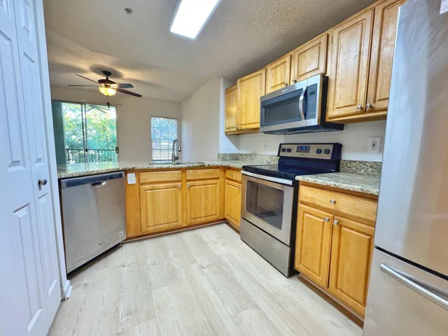 a kitchen with stainless steel appliances granite countertop wooden cabinets a sink a stove a refrigerator a microwave oven with cabinets and wooden floor