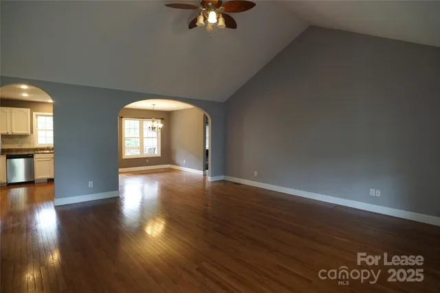 an empty room with wooden floor chandelier fan and windows