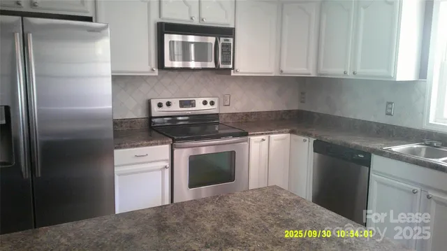 a kitchen with stainless steel appliances granite countertop a refrigerator a stove a sink and white cabinets