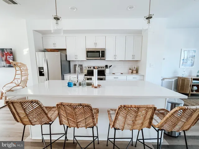 a kitchen with stainless steel appliances kitchen island granite countertop a dining table chairs and a refrigerator