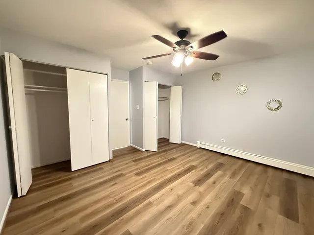 a view of an empty room with wooden floor and a ceiling fan
