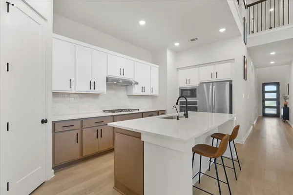 a kitchen with stainless steel appliances granite countertop a sink a stove a refrigerator and white cabinets with wooden floor