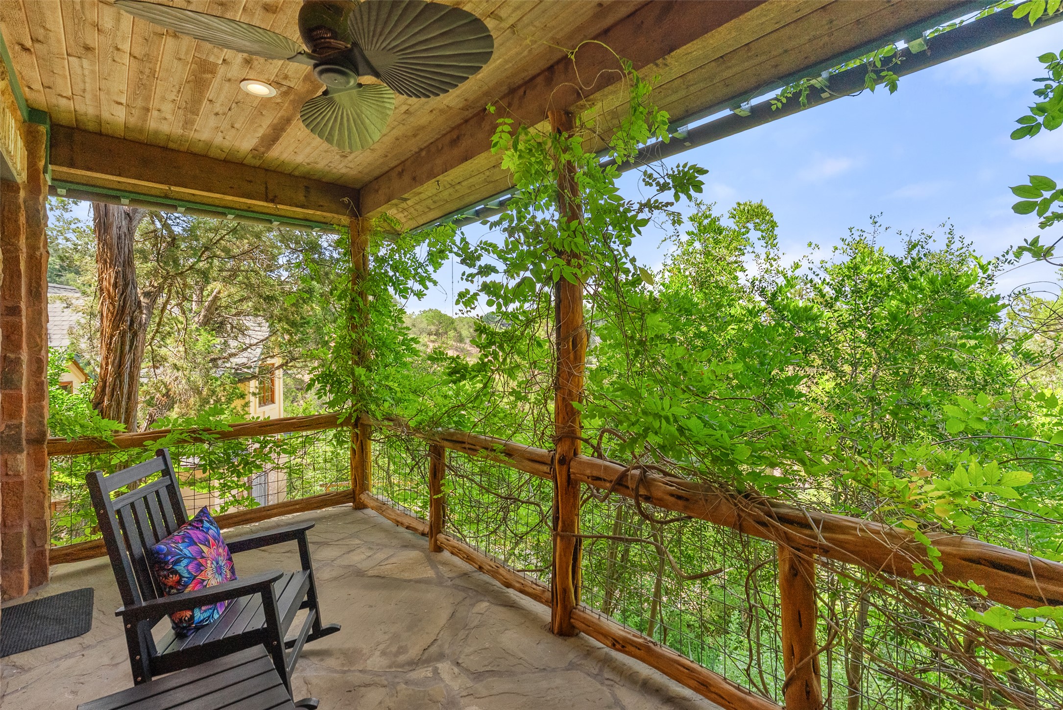 1354 The High Road Austin, TX 78746 - Photo 24 of 40 Enjoy nature's embrace from this charming covered patio of the primary suite, featuring rustic wood railings and a stone floor.