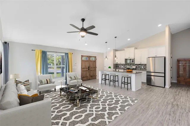 a living room with stainless steel appliances furniture a rug and a kitchen view