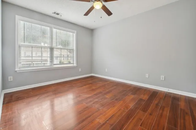 an empty room with wooden floor chandelier fan and windows