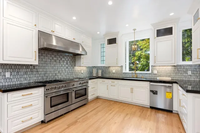 a large kitchen with stainless steel appliances a large counter top a stove a refrigerator and white cabinets