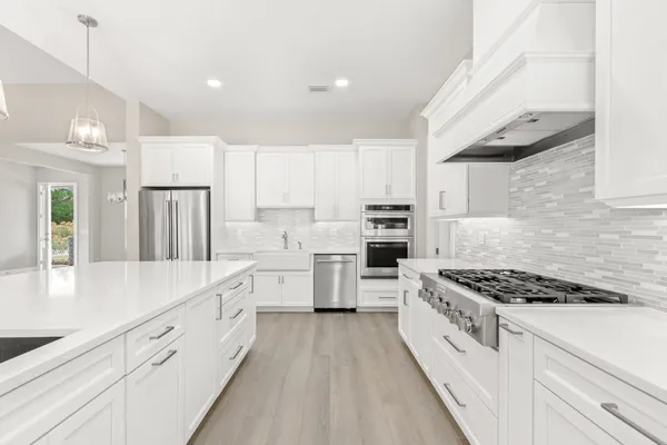 a kitchen that has a lot of white cabinets and stainless steel appliances