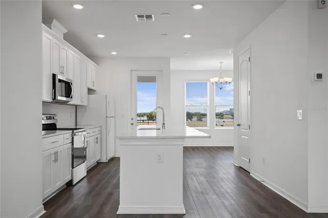 a kitchen with stainless steel appliances a microwave a stove a sink dishwasher a refrigerator white cabinets and wooden floor next to a window