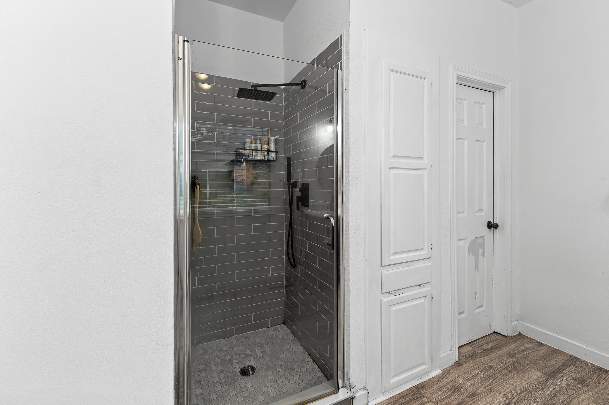 11737 Rydalwater Lane Austin, TX 78754 - Photo 20 of 40 Glass-enclosed shower featuring gray subway tile walls and hexagon tile flooring, with a dark-finish rainfall showerhead and handheld sprayer