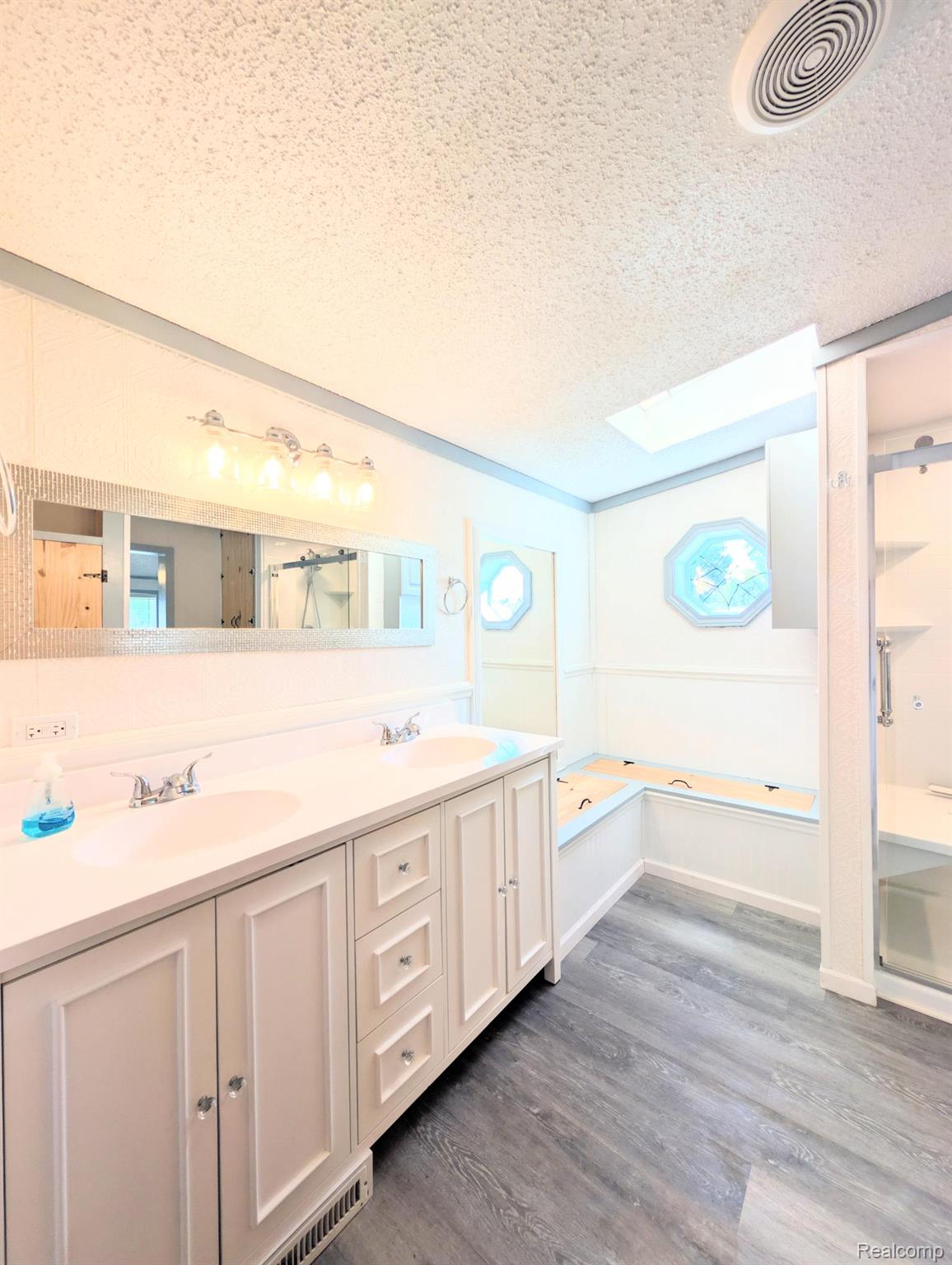 169 Post Branch Fenton, MI 48430 - Photo 14 of 19 Double vanity with integrated sinks, built-in soaking tub, wood-finish flooring, and natural light from a skylight