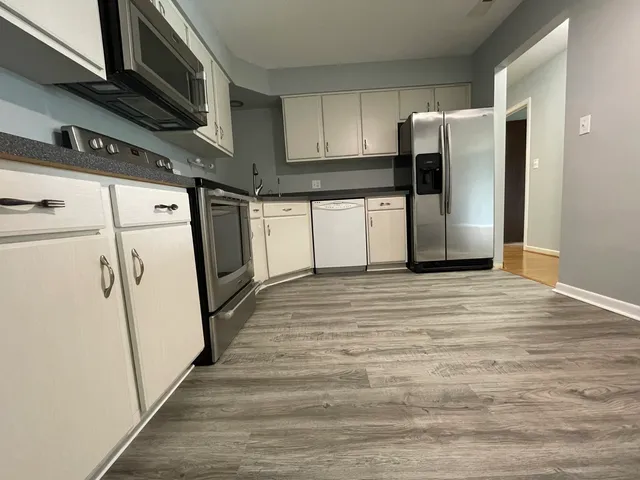 a view of a refrigerator in kitchen and an empty room with wooden floor