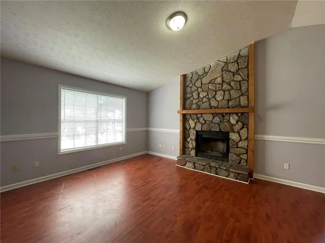 an empty room with wooden floor fireplace and windows