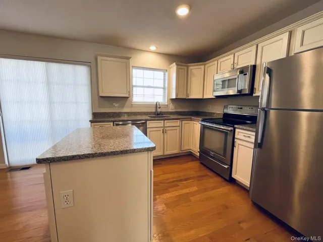 a kitchen with stainless steel appliances granite countertop a refrigerator a sink dishwasher a stove with white cabinets and wooden floor