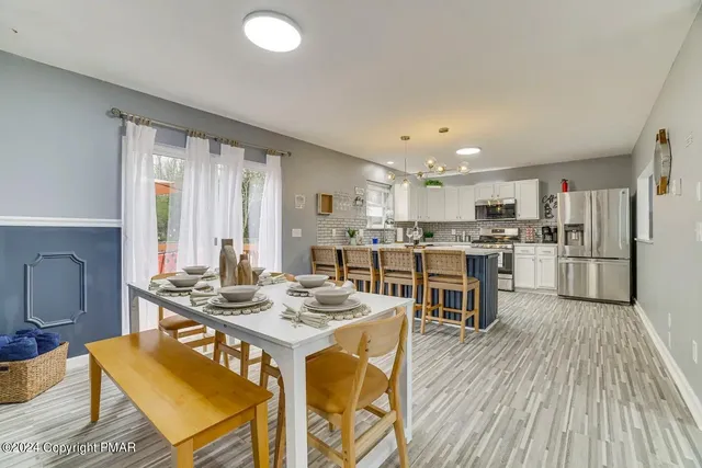 a open dining room with stainless steel appliances kitchen island granite countertop a refrigerator a stove a sink dishwasher with a dining table and chairs with wooden floor