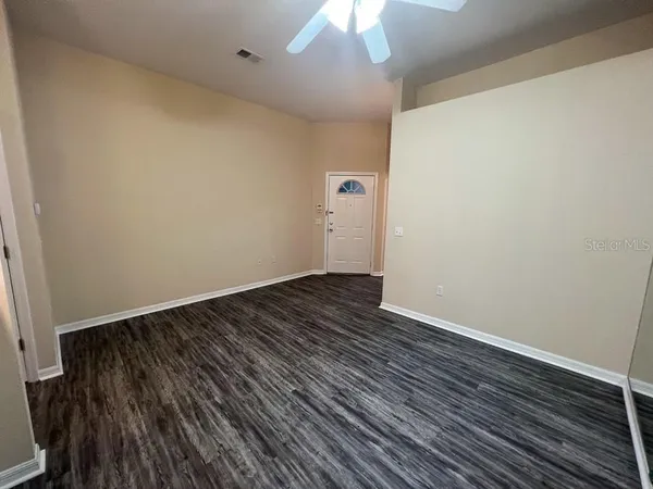 a view of an empty room with wooden floor and a ceiling fan