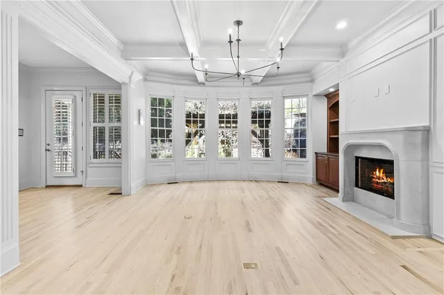 an empty room with wooden floor fireplace chandelier and windows